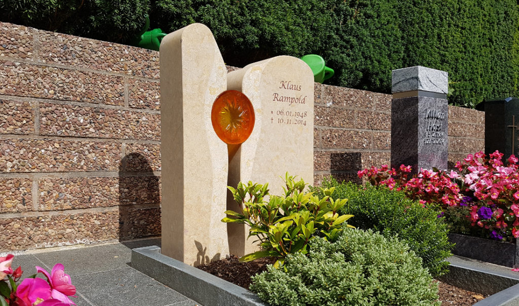 Zweiteiliger Urnengrabstein aus Sandstein mit eingelassener Sonne aus Glas.