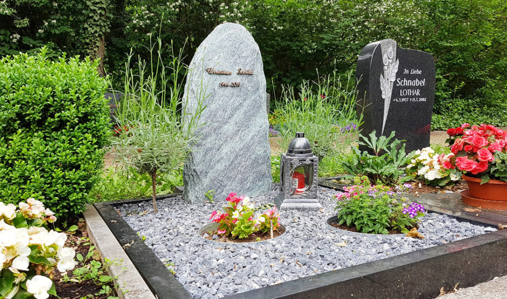 Grabstein in Form eines Findlings auf dem pflegeleicht gestalteten Urnengrab mit Kies.