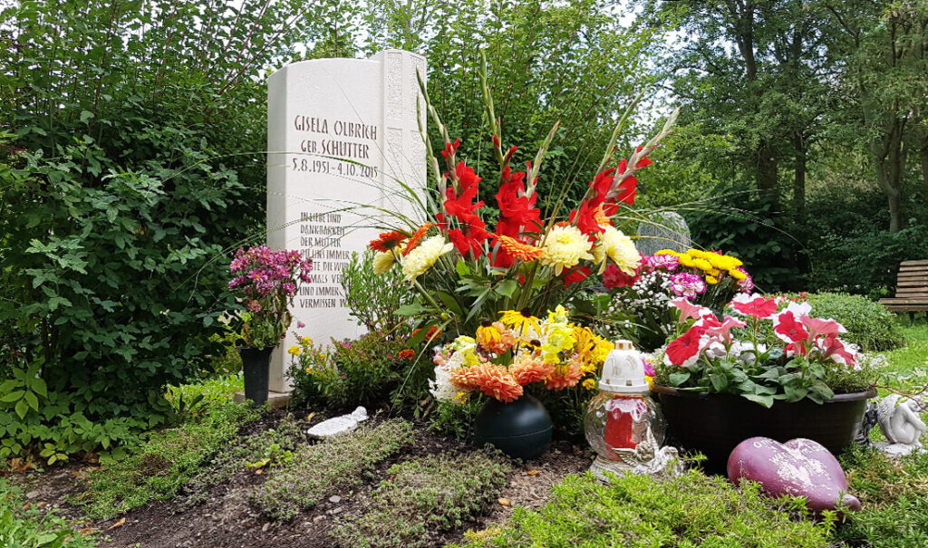 Einzelgrab gestaltet mit vielen farbenfrohen Trauergestecken und Trauersträußen in Vasen und Schalen.