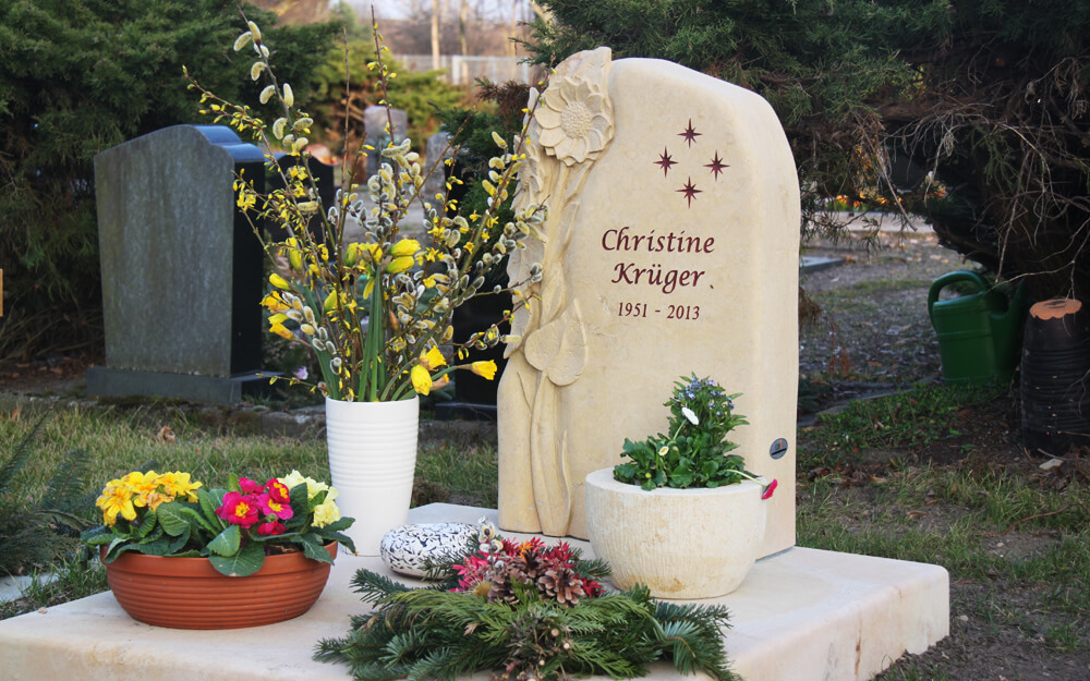 Heller Urnengrabstein mit Grabplatte und winterlicher Grabgestaltung