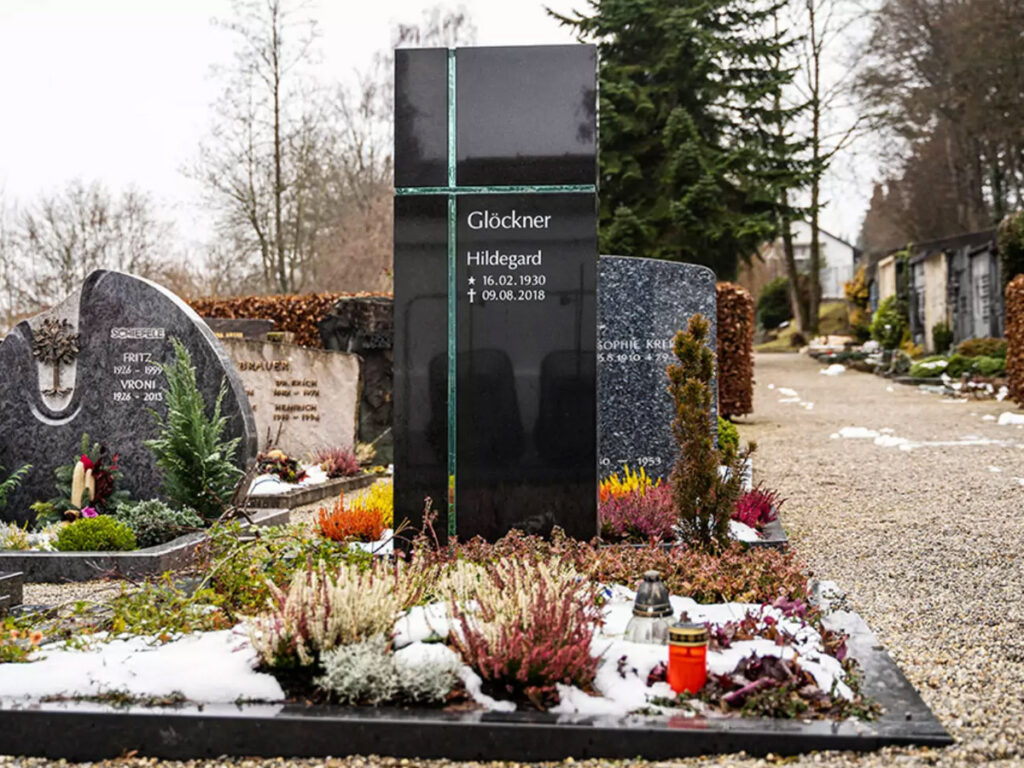 Modernes Einzelgrab mit schwarzem Granitgrabstein und christlichem Kreuz-Symbol aus Glas - winterliche Grabbepflanzung mit Bodendeckern und kleinen Stauden