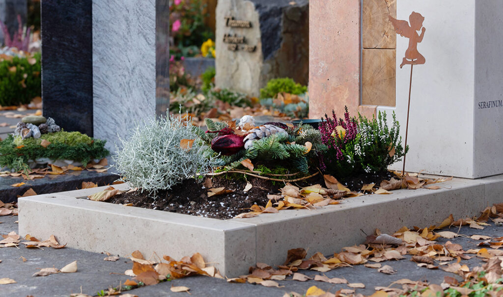 Einfache Urnengrab-Gestaltung im Winter mit einem großen Gesteck aus Tannenzweigen und winterharten Pflanzen.