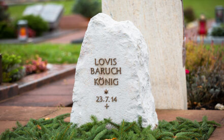 Rustikaler Grabstein Felsen / Findling in hellem Kalkstein mit winterlicher Grabgestaltung & Reisig