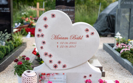 Impressionen vom Friedhof: Grabstein als Herz mit Einfassung und Sockel aus hellem Kalkstein mit gravierten Blüten