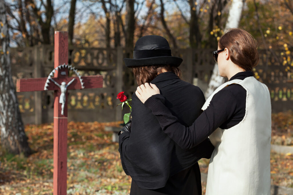 Zwei trauernde Angehörige vor einem Grab des Verstorbenen