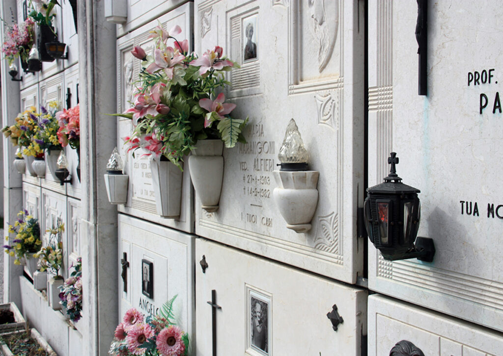 Urnenwand mit dekorativen Grabplatten und Grabinschriften auf einem Friedhof in Italien.