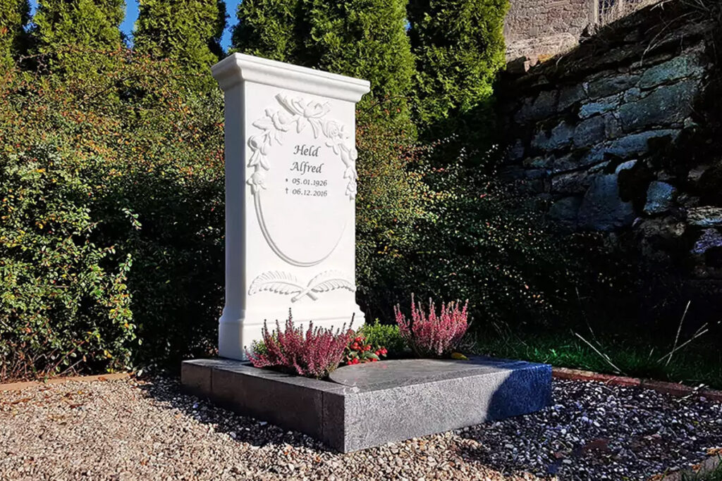 Grab im Halbschatten mit Grabstein aus Marmor und runder Grabplatte mit Ausschnitt für Pflanzen.