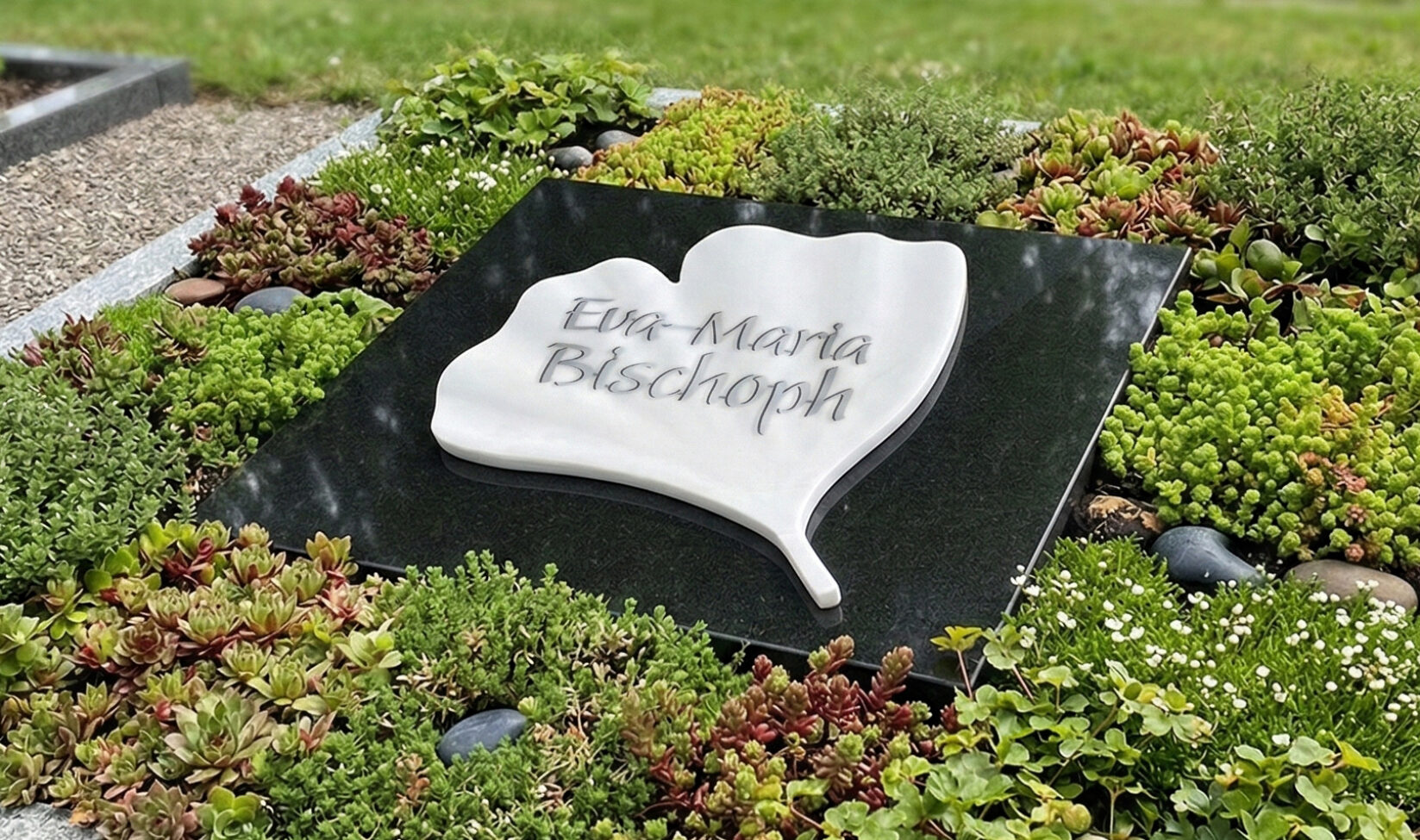 Liegeplatte aus dunklem Granit als günstiger Grabstein mit einem Ginkgoblatt aus weißem Granit
