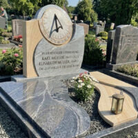 Die Grabplatten präsentieren sich als eine moderne  mehrteilige Komposition aus geschwungenen Formen und kontrastierenden Materialien  die sich harmonisch in ein feines graues Kiesbett einfügen. Sie sind nicht flach  sondern weisen unterschiedliche Höhen und Überlappungen auf  was dem Design Tiefe verleiht.