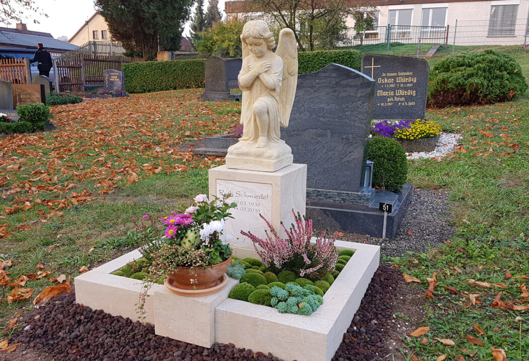 Im Hintergrund leuchten herbstlich verfärbte Bäume und unterstreichen die friedliche Atmosphäre des Friedhofs.