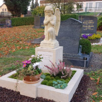 Im Hintergrund leuchten herbstlich verfärbte Bäume und unterstreichen die friedliche Atmosphäre des Friedhofs.