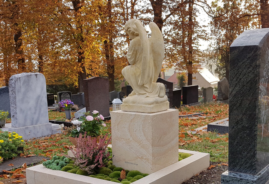 Die Grabanlage zeichnet sich durch eine moderne  stufenförmige Einfassung aus hellem Naturstein aus  die einen harmonischen Kontrast zum dunklen Kies des Weges bildet.