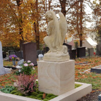 Die Grabanlage zeichnet sich durch eine moderne  stufenförmige Einfassung aus hellem Naturstein aus  die einen harmonischen Kontrast zum dunklen Kies des Weges bildet.