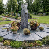 Eine Grabstele mit trauerndem Engel ist das zentrale Gestaltungselement. 