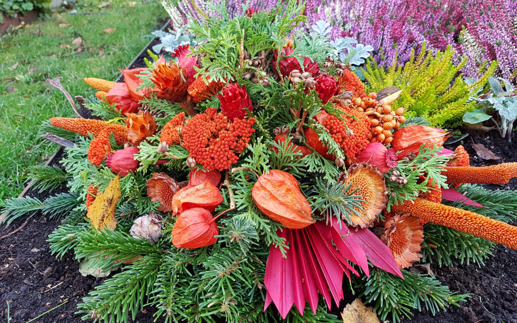 Farbakzente wie leuchtendes Orange setzen Lampionblumen und verschiedene eingefärbte Trockenblumen im Gesteck.